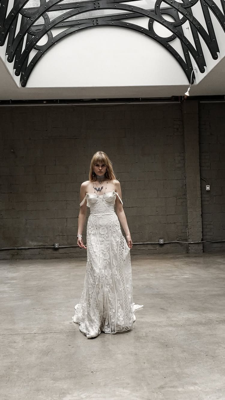 2026 Wedding Dresses: 12 Bridal Styles to Know Right Now 5 Woman in a white lace wedding dress with a structured corset bodice standing in an industrial room.