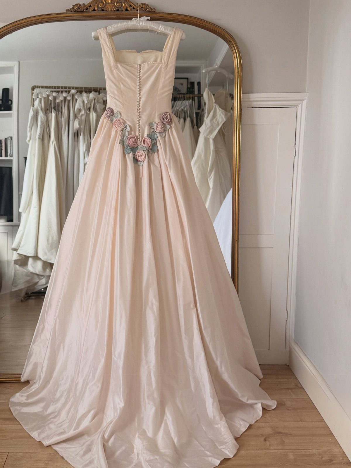 2026 Wedding Dresses: 12 Bridal Styles to Know Right Now 2 A pale pink wedding gown with floral appliqués hanging in front of a gold mirror.