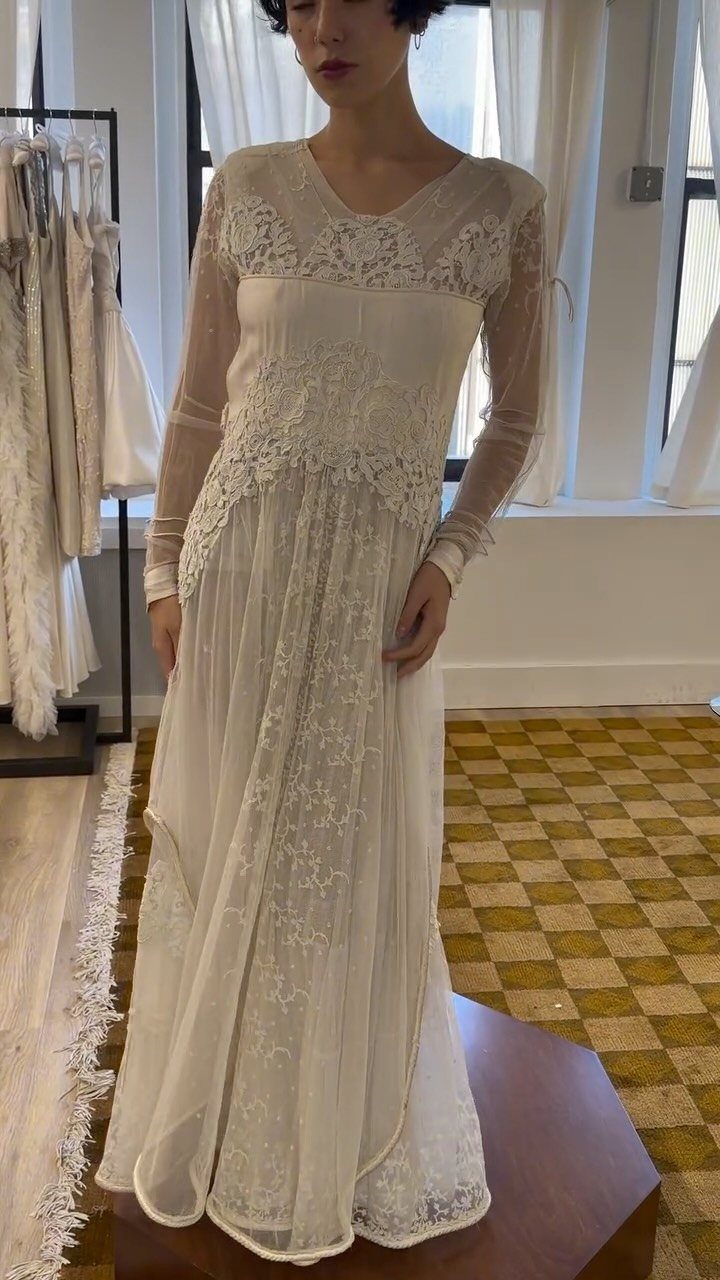 2026 Wedding Dresses: 12 Bridal Styles to Know Right Now 7 A woman wearing a long-sleeved cream wedding dress with intricate lace detailing and floral patterns.