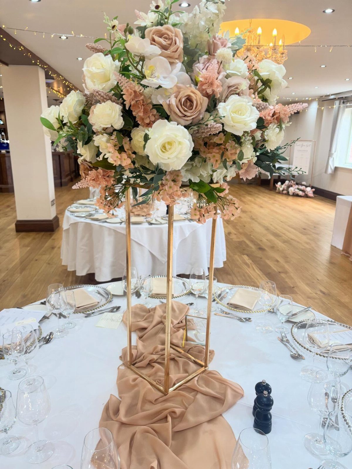 Blush Wedding Colors: 9 Palettes That Work at Actual Weddings 9 Large blush and white floral arrangement on a gold stand with champagne fabric on a wedding table.