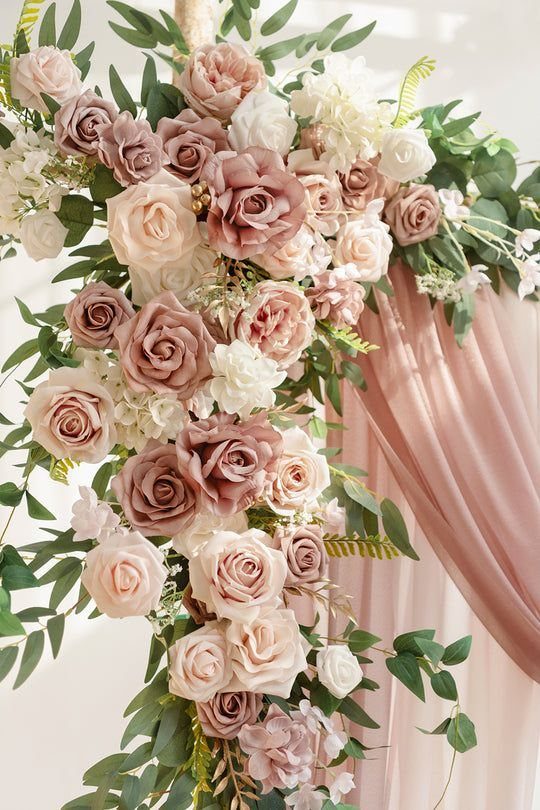Blush Wedding Colors: 9 Palettes That Work at Actual Weddings 8 Blush and dusty rose floral arrangement with green leaves against pink fabric backdrop.