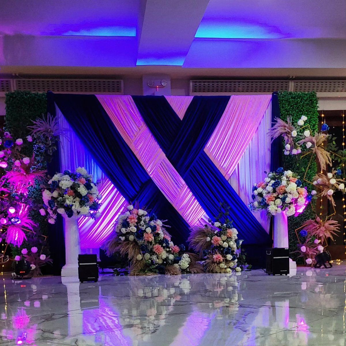 Blush Wedding Colors: 9 Palettes That Work at Actual Weddings 2 Navy blue and pink draped fabric backdrop with various floral arrangements on a polished floor.