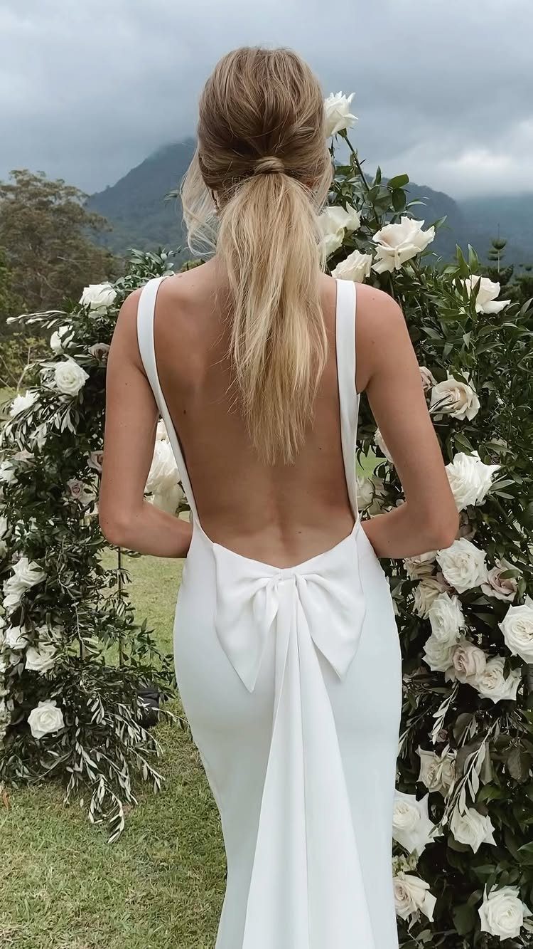 Woman in a white wedding dress with a large bow on the back standing before roses.