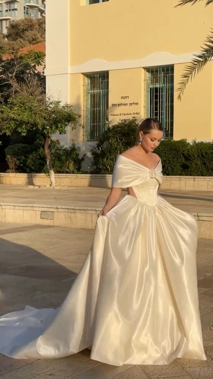 A woman wearing an ivory satin wedding dress with a bow detail on the bodice.
