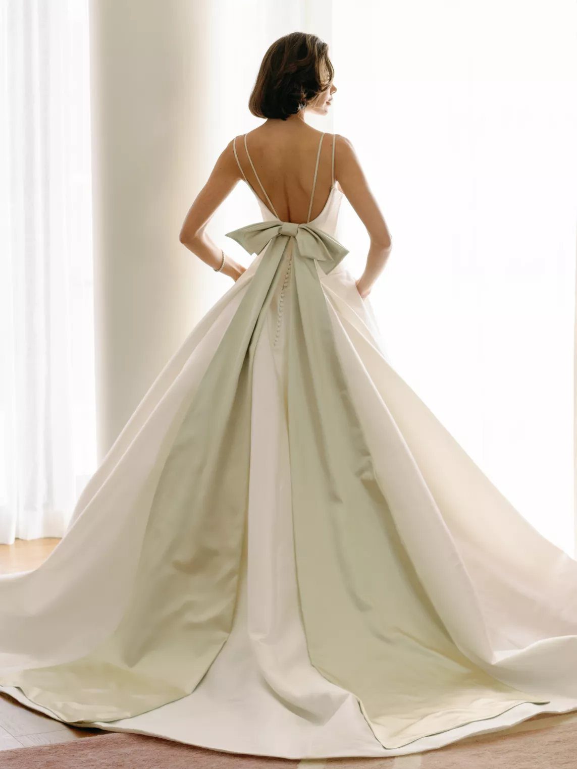 Woman in a white satin wedding dress with a large bow at the waist and long train.
