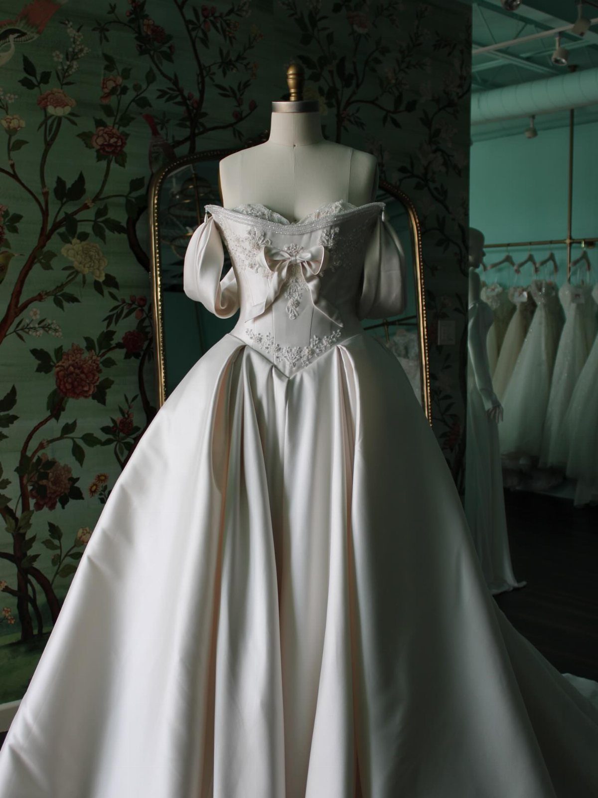 An ivory satin wedding dress with a small bow on the neckline displayed on a mannequin.