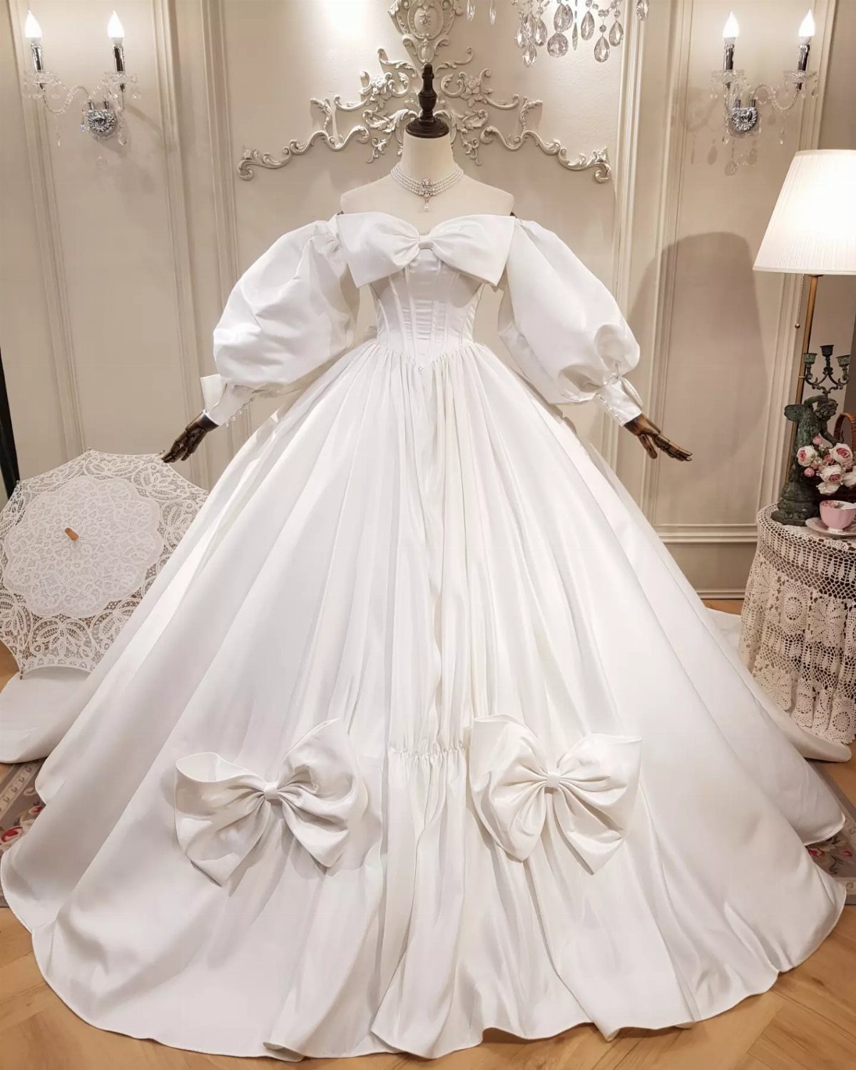 White satin wedding dress on a mannequin with large puff sleeves and decorative bows on the skirt.