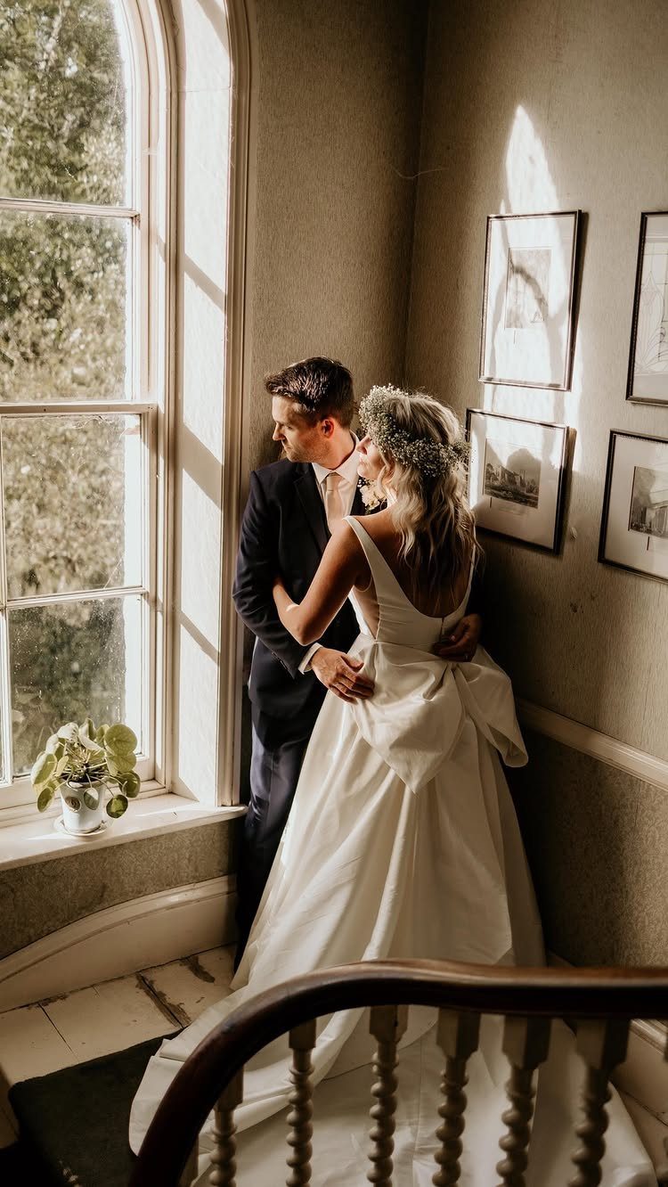 A bride wearing a white wedding dress with a large bow on the back stands with her groom.
