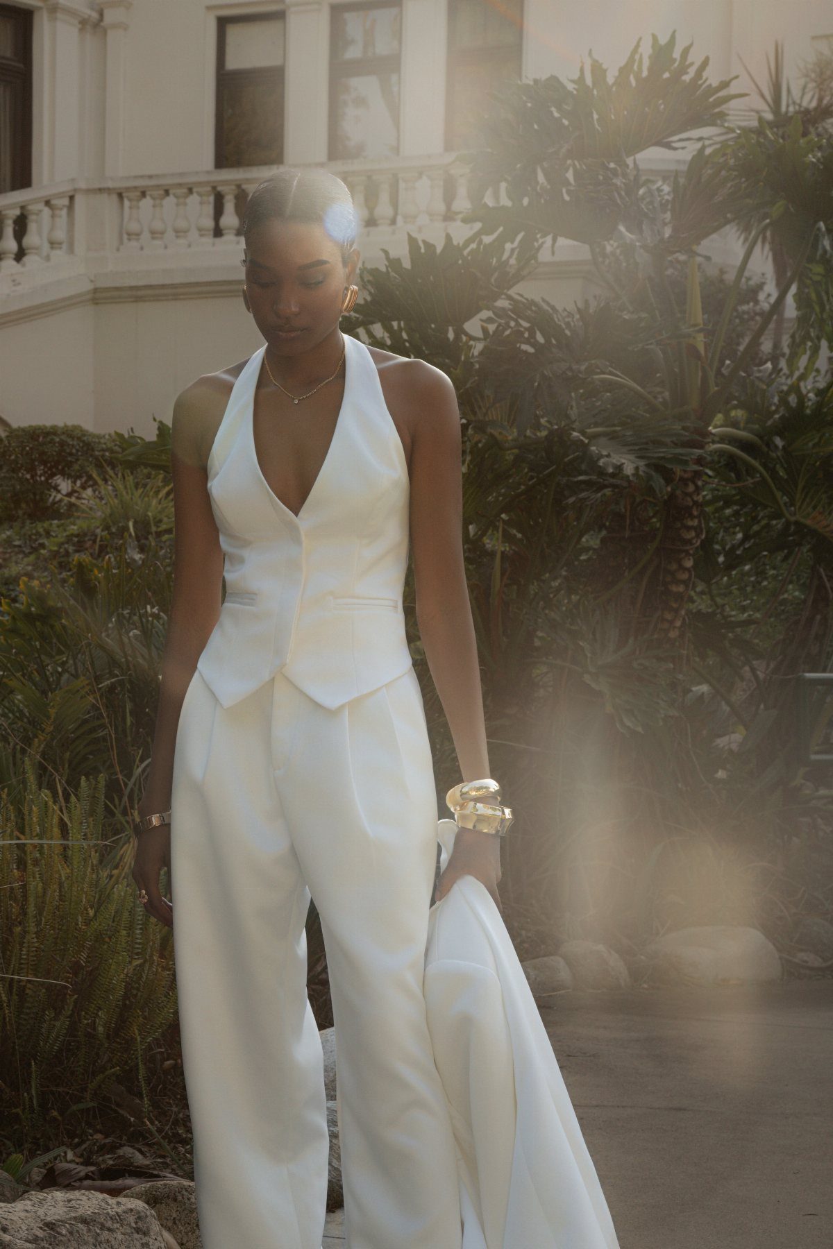Woman wearing a white satin halter waistcoat and matching wide-leg trousers standing outdoors.