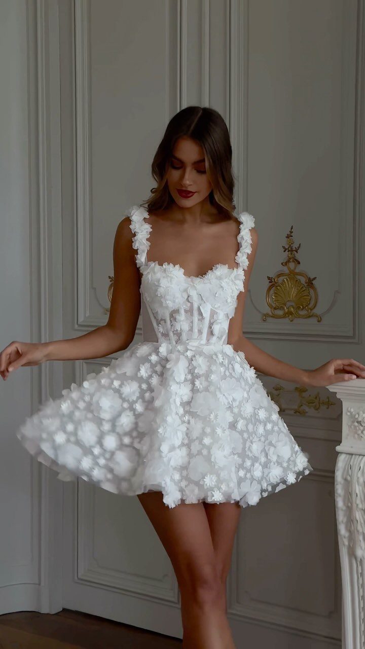 A woman wearing a white textured floral mini dress standing against white paneled walls.