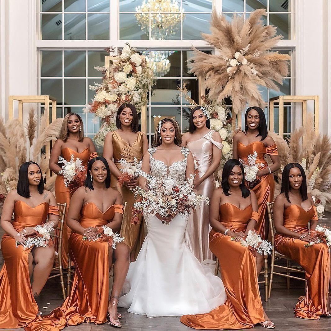 Bridesmaids in burnt orange satin dresses posing with a bride in a white wedding gown.