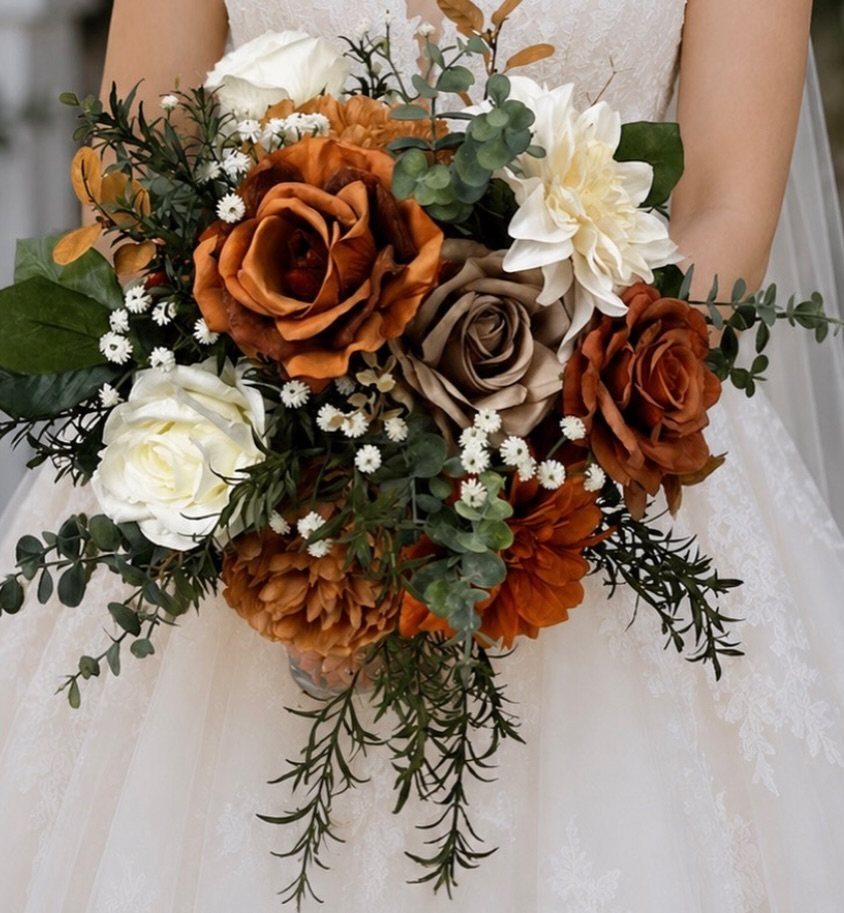A bridal bouquet with burnt orange and cream roses accented by green eucalyptus leaves.