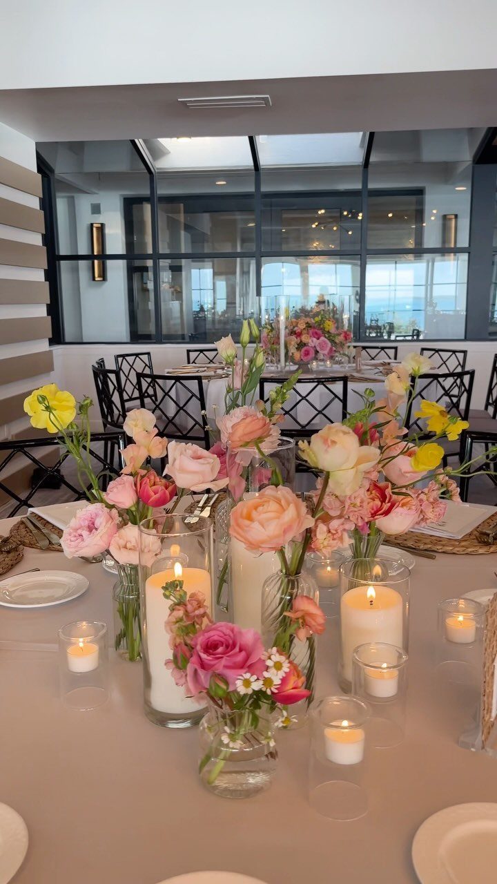 Floral arrangements in glass vases surrounded by white pillar candles on a dining table.
