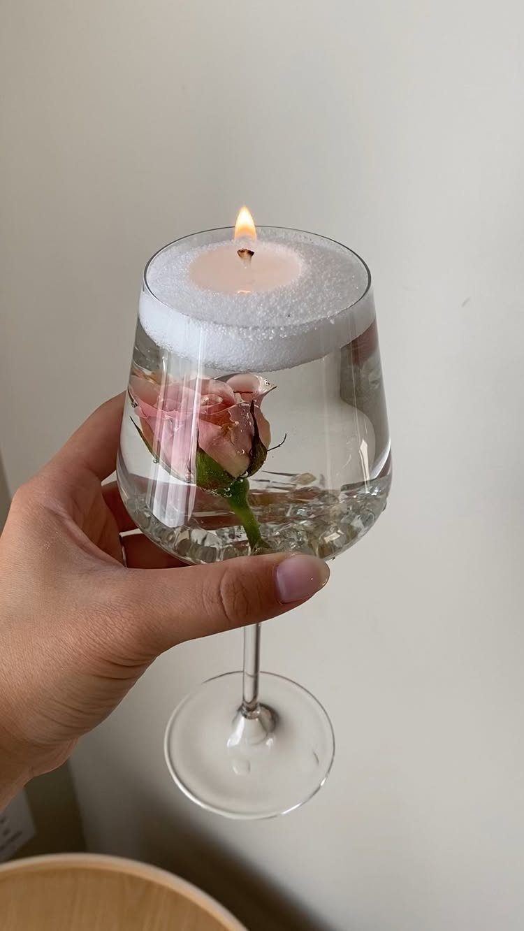 A hand holding a wine glass with a submerged rose and a floating candle.
