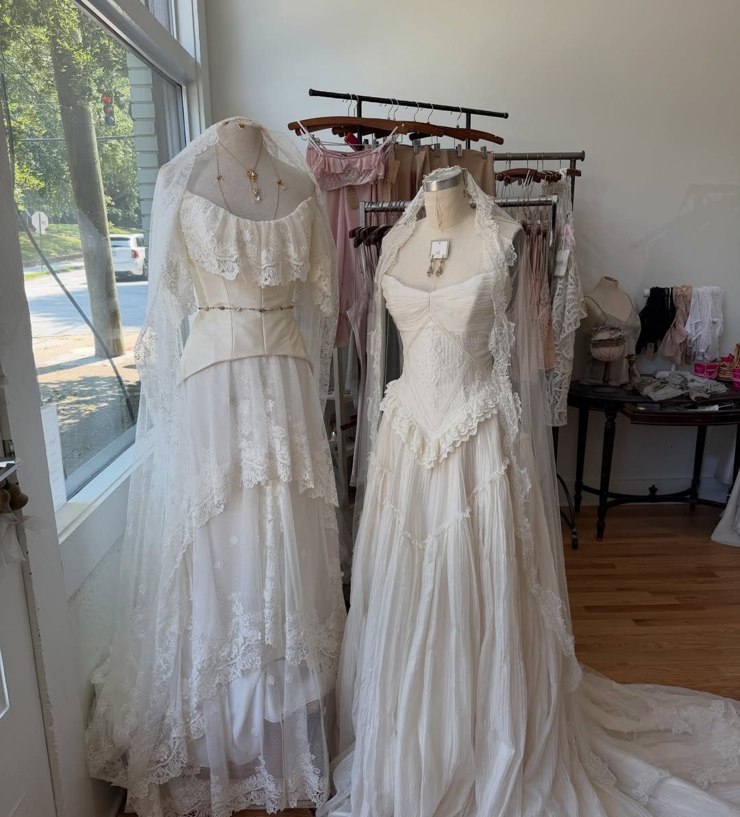 6 Classy Vintage Wedding Dress Finds That Hold Up 1 Two white lace vintage wedding dresses displayed on mannequins inside a bright boutique shop.