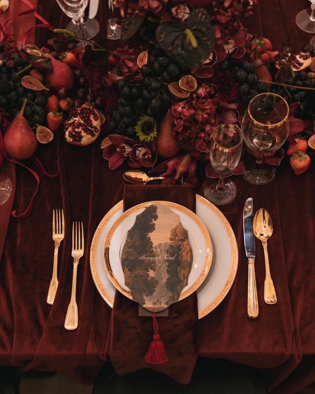 Dark Red Wedding Colors: 20 Ideas for Mood and Palette 10 A formal wedding table set with burgundy velvet, gold utensils, and dark red fruit centerpieces.