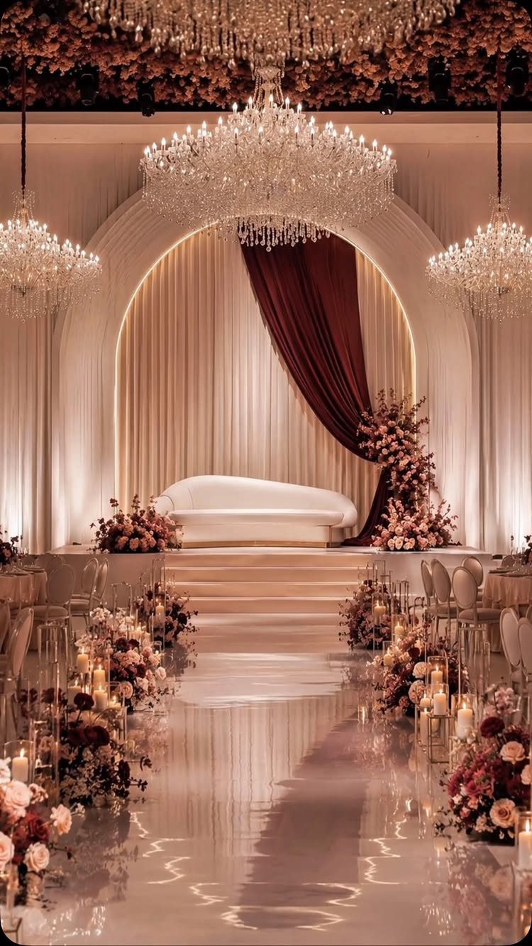 Dark Red Wedding Colors: 20 Ideas for Mood and Palette 11 Wedding ceremony aisle lined with blush and dark red floral arrangements under large crystal chandeliers.