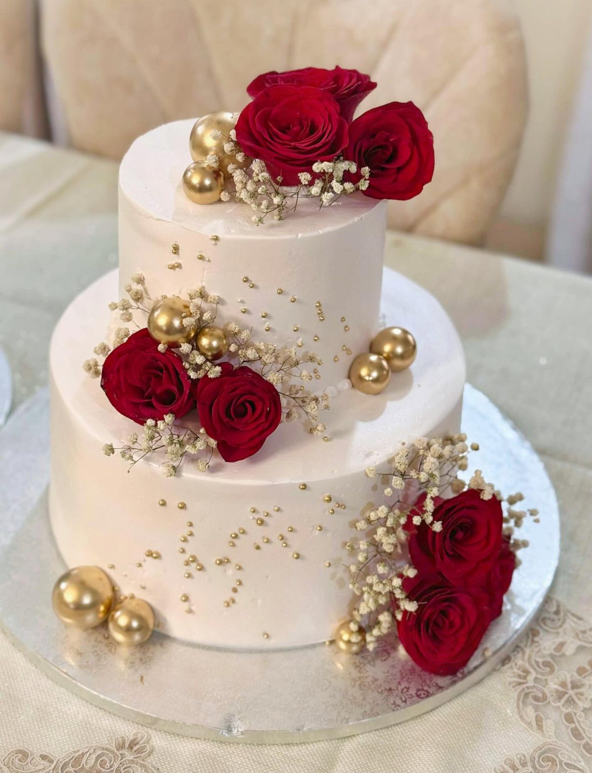 Dark Red Wedding Colors: 20 Ideas for Mood and Palette 16 Two-tier white wedding cake decorated with deep red roses, baby's breath, and gold spheres.