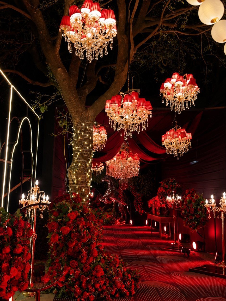 Dark Red Wedding Colors: 20 Ideas for Mood and Palette 14 Red rose arrangements and crystal chandeliers hanging from trees at a dark red wedding event.