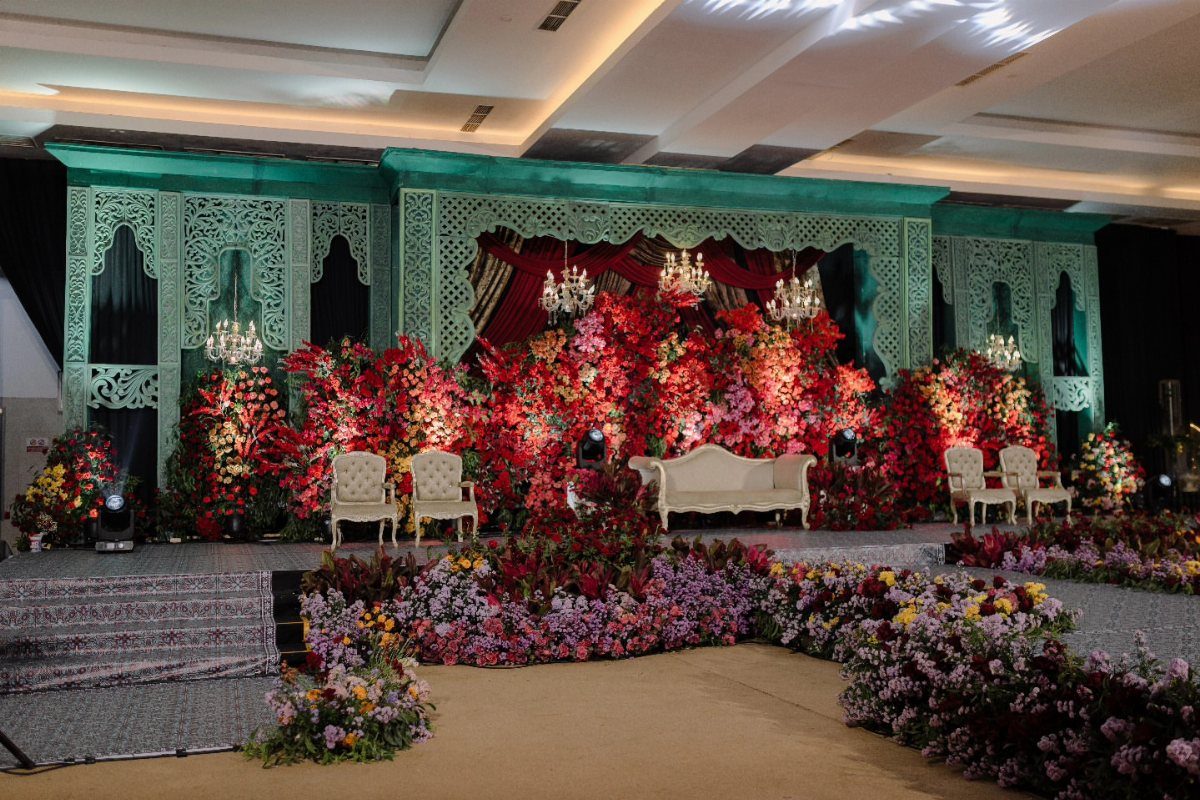 Dark Red Wedding Colors: 20 Ideas for Mood and Palette 8 Large wedding stage featuring massive red floral arrangements with green foliage and teal backdrops.