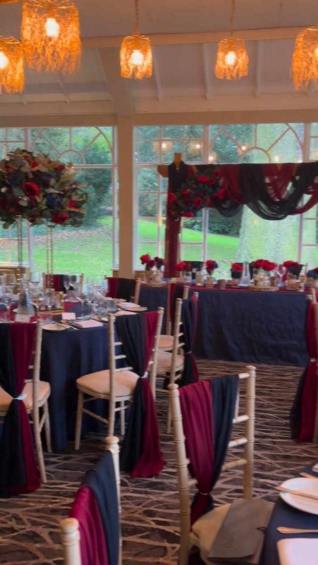 Dark Red Wedding Colors: 20 Ideas for Mood and Palette 12 Wedding reception tables with navy tablecloths, burgundy chair drapes, and deep red floral centerpieces.
