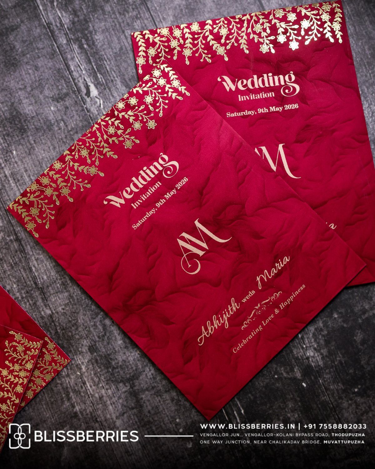 Dark Red Wedding Colors: 20 Ideas for Mood and Palette 7 Two deep red wedding invitations with gold floral patterns resting on a dark wooden surface.