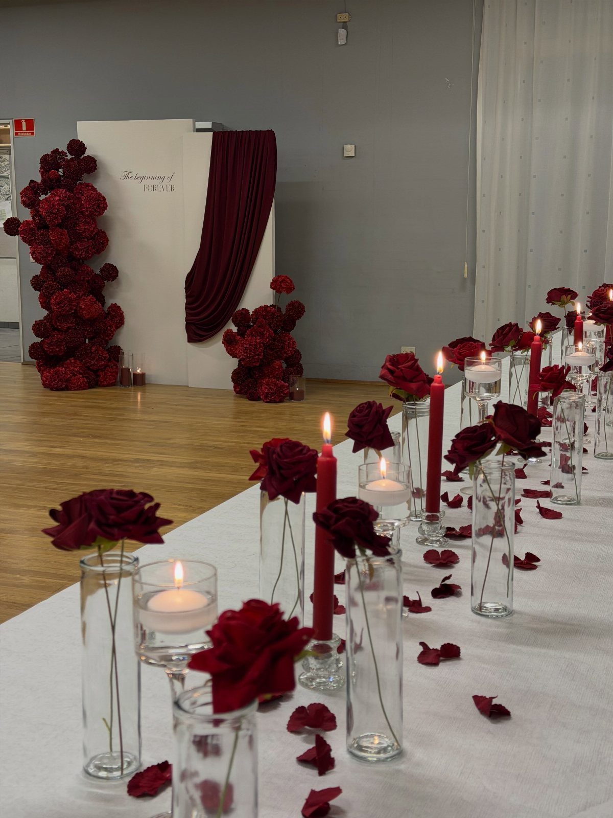 Dark Red Wedding Colors: 20 Ideas for Mood and Palette 3 Red roses in glass vases and red taper candles on a white tablecloth with rose petals.
