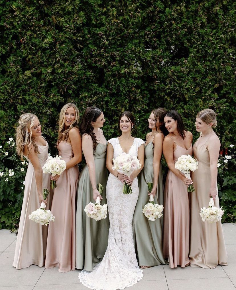 Bridesmaids in dusty rose and sage green satin dresses posing with a bride outdoors.