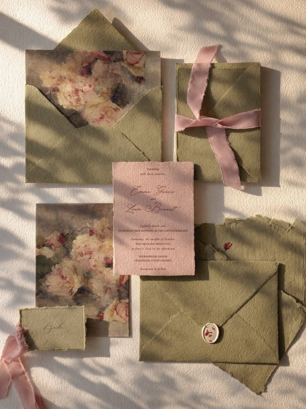 Dusty rose wedding invitations and sage green envelopes arranged with pink ribbon and wax seal.