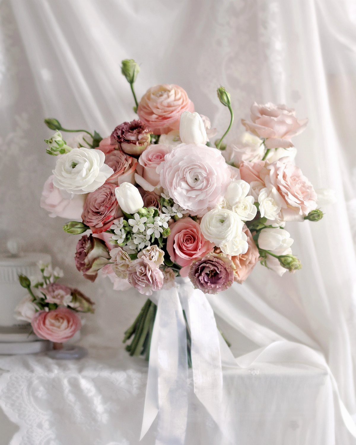 Dusty rose and cream floral bouquet with white silk ribbons on a lace table.