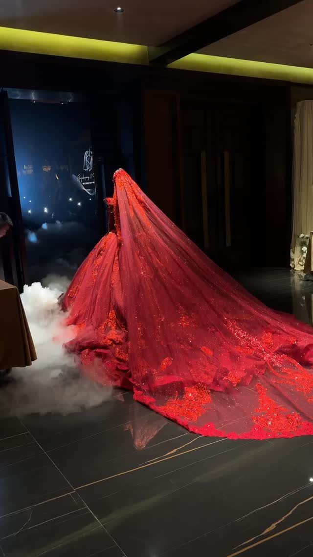 A person in a dramatic, voluminous red gown with a long train amidst white fog.