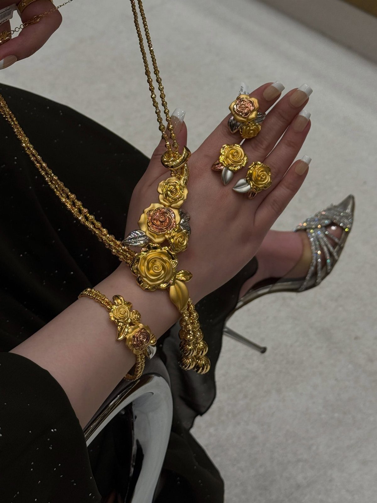 Person wearing a gold floral jewelry set with rose-shaped necklace, bracelet, and rings.