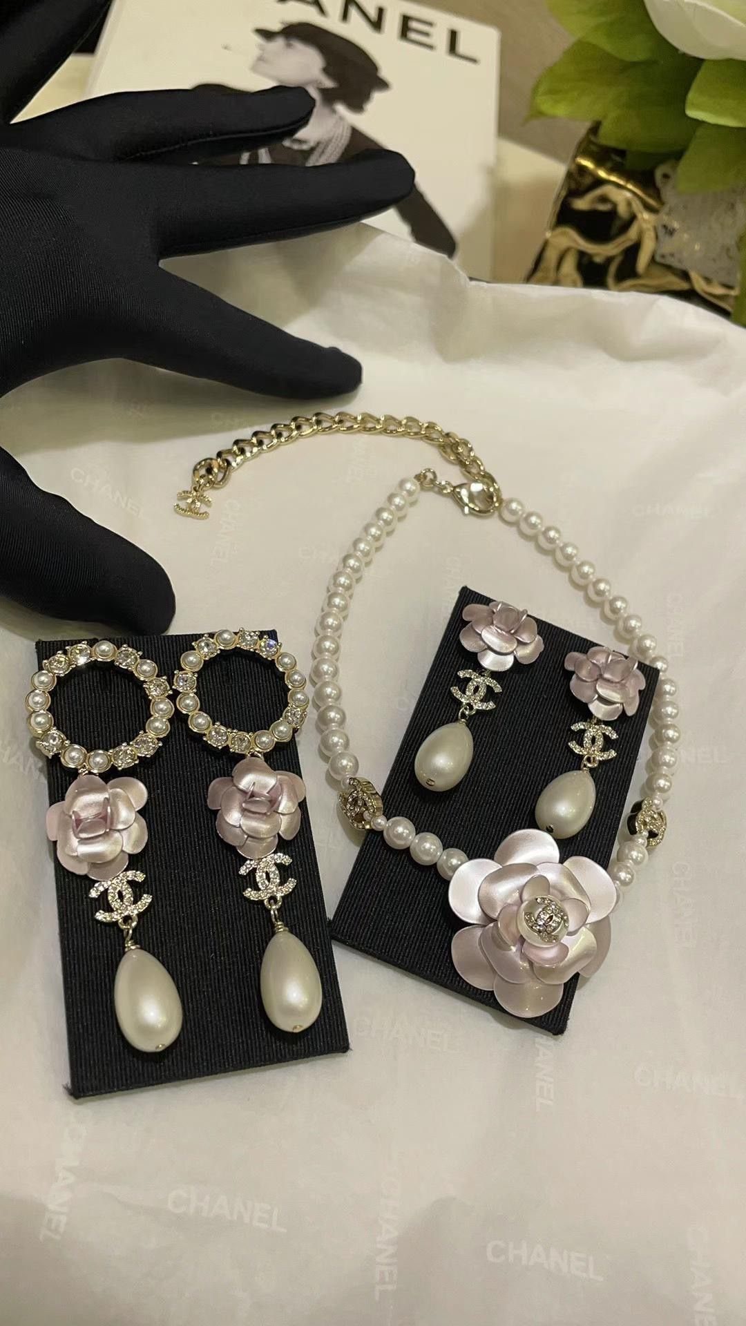 A pearl and floral jewelry set displayed on black stands with Chanel branding.