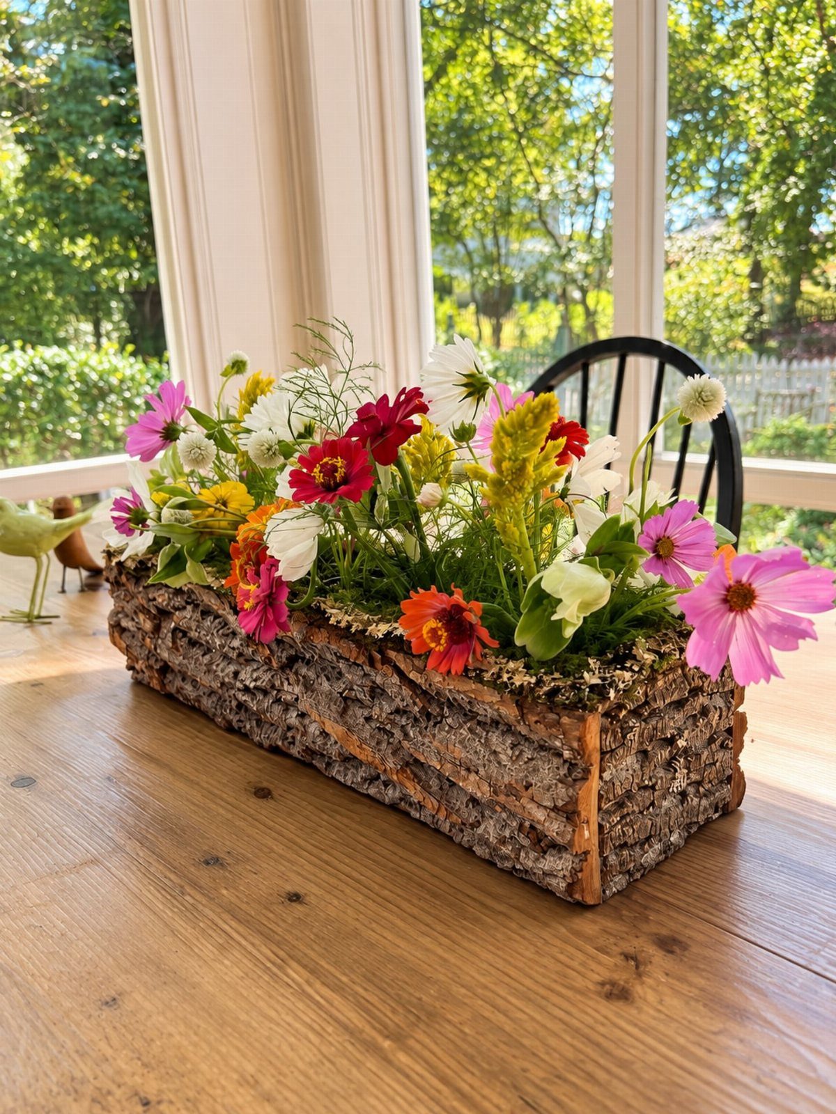 A bark-covered rectangular planter filled with vibrant colorful wildflowers on a wooden table.