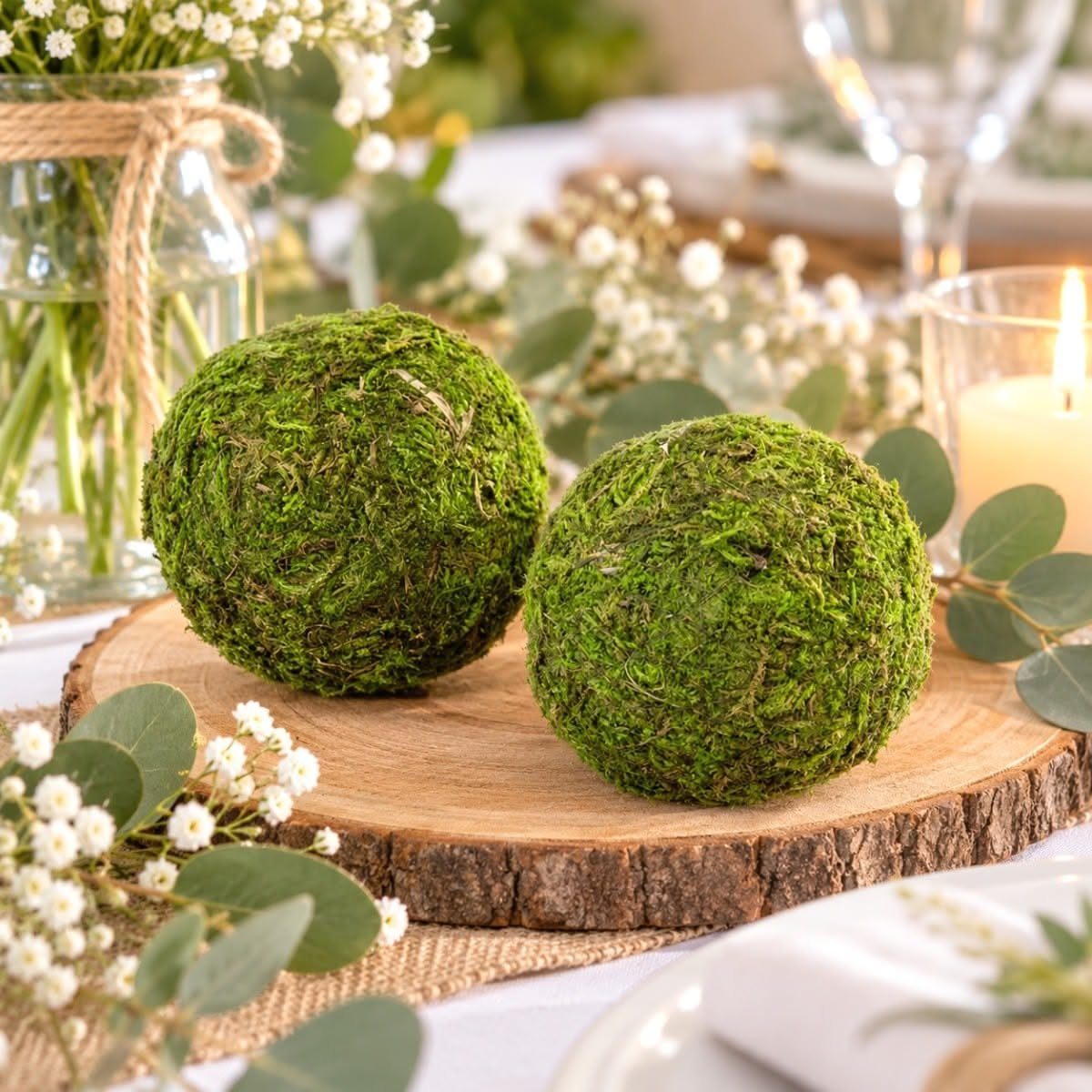 Two round green moss balls resting on a wooden slice centerpiece on a decorated table.