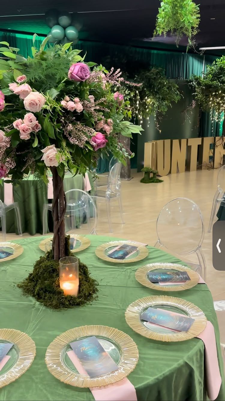 Tall floral centerpiece with pink roses and greenery on a mossy base at a green themed table.