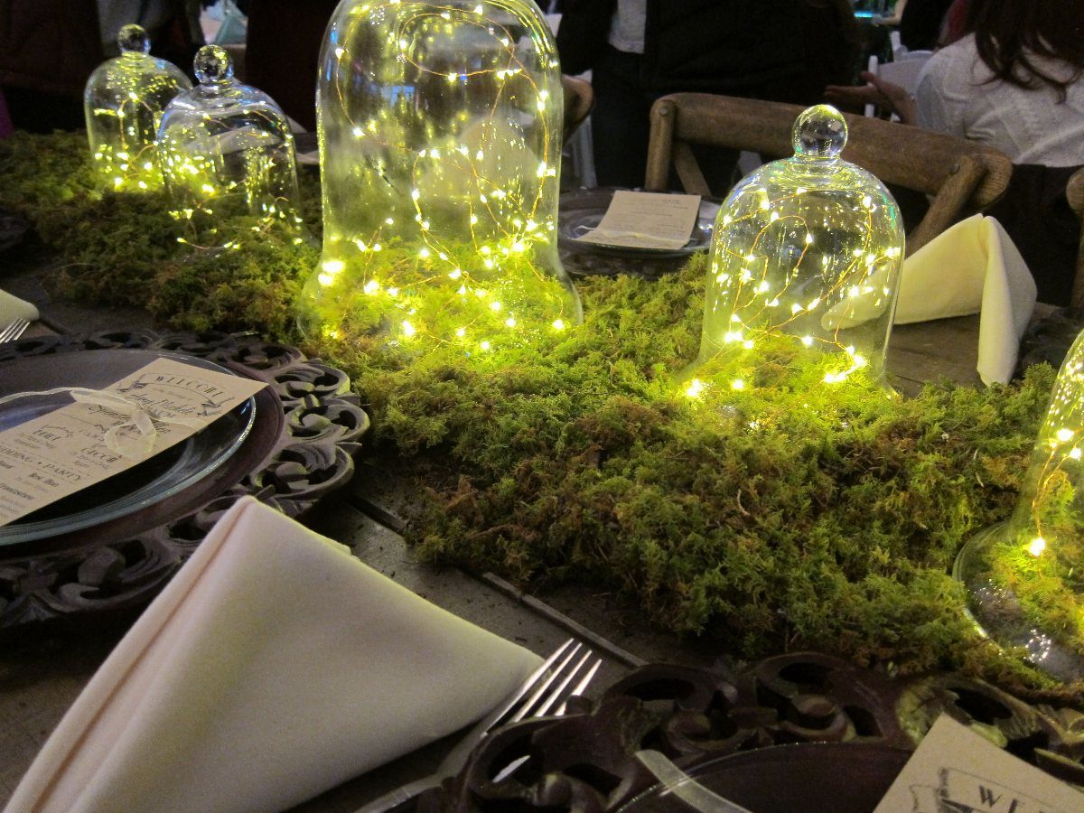 Glass cloches filled with glowing fairy lights resting on a bed of green moss on a table.