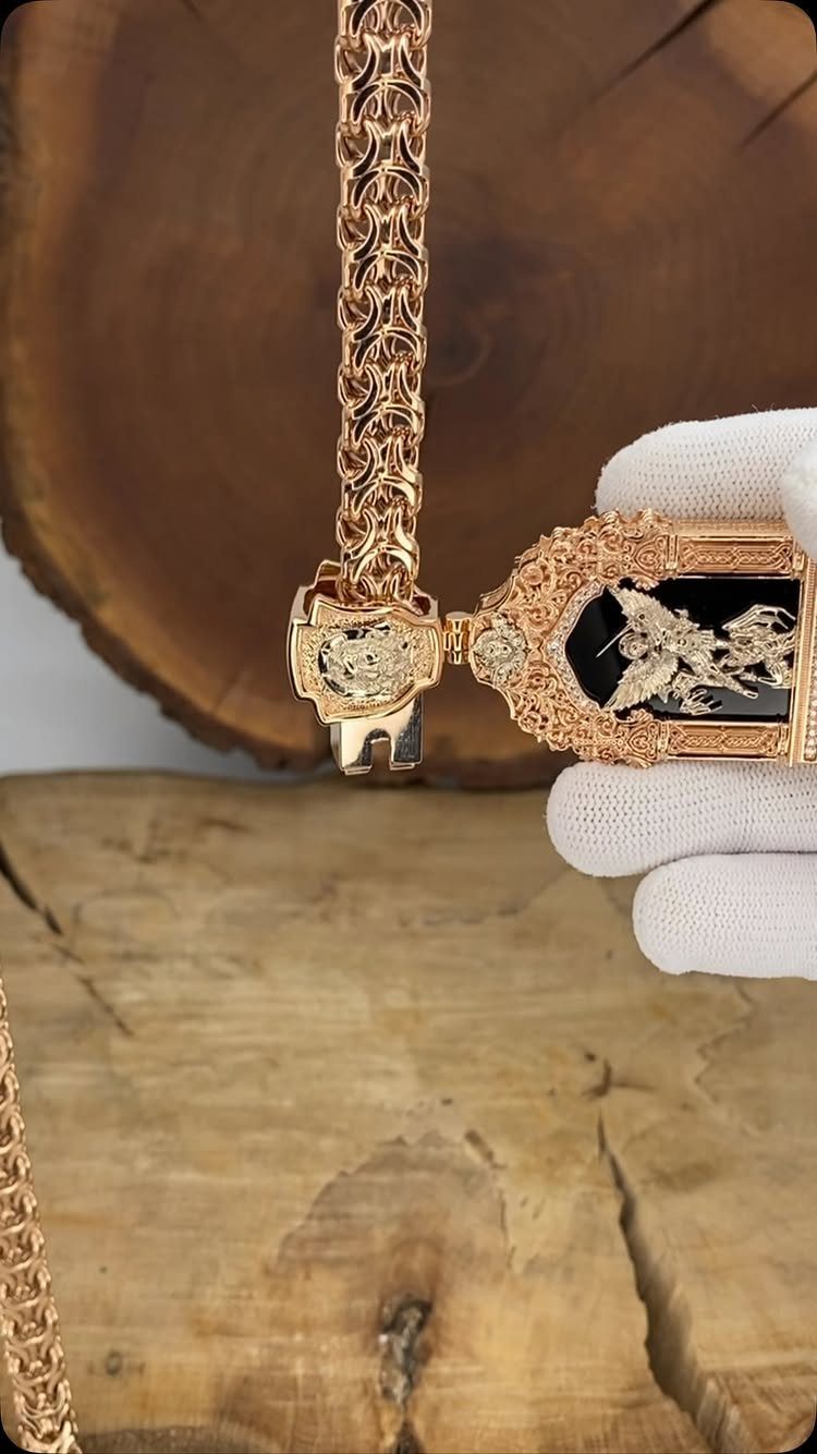 A rose gold Byzantine chain with intricate interwoven links held by a gloved hand.