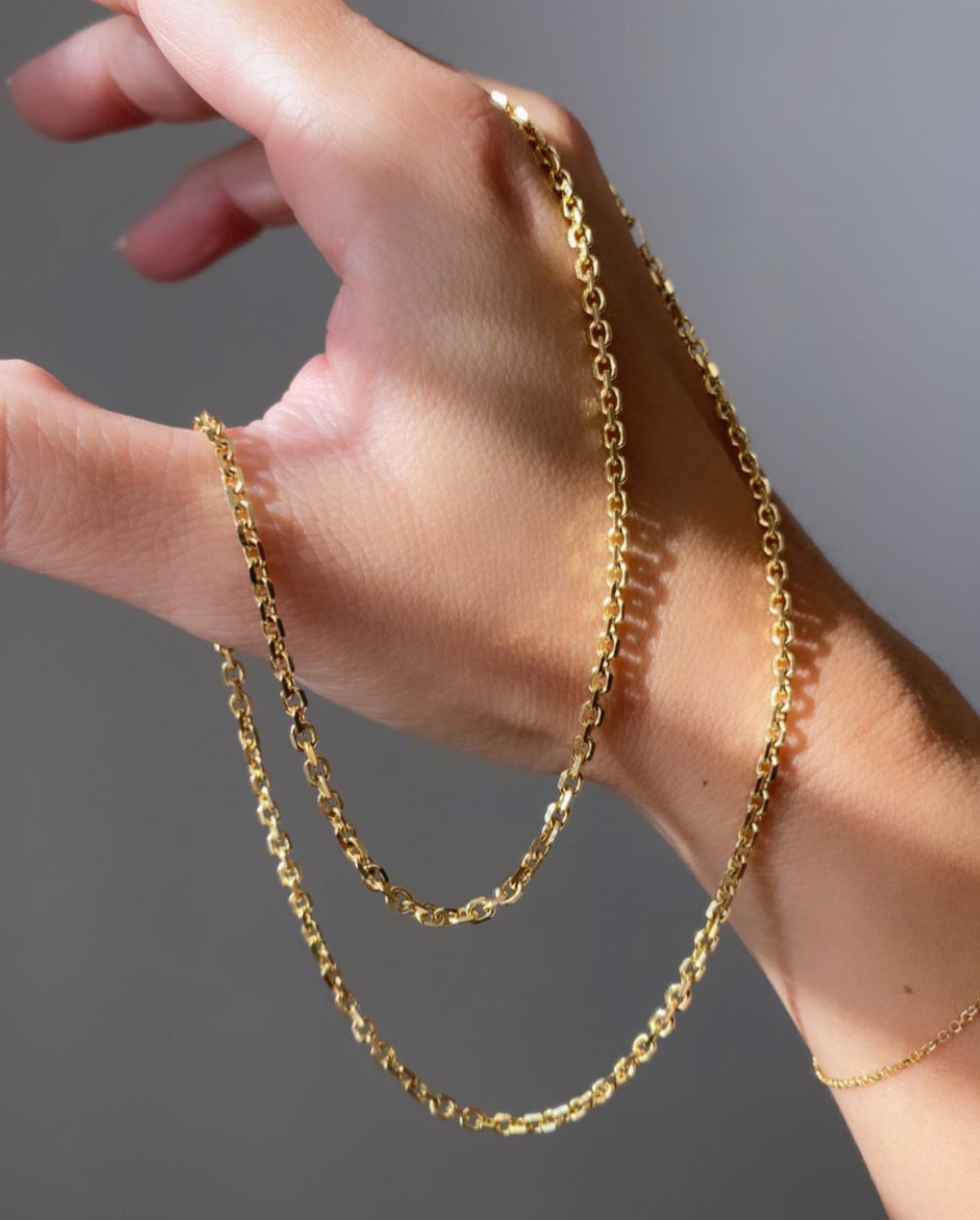 A delicate gold cable chain draped elegantly over a person's hand and wrist.