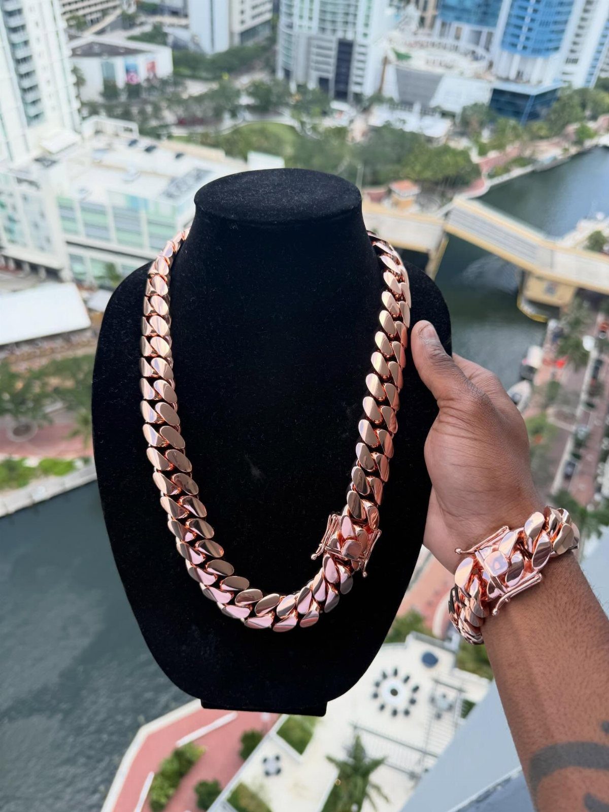 Rose gold Cuban link chain necklace on a black bust held against a city skyline.