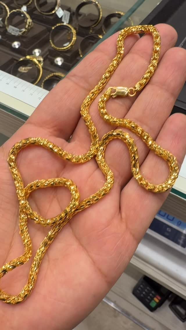 A textured gold diamond cut chain resting on an open human hand in a jewelry store.