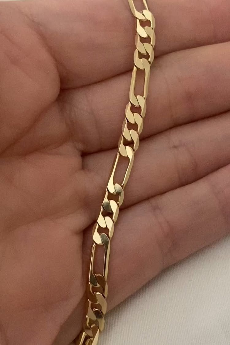 A gold Figaro chain with alternating link lengths held in a person's hand.
