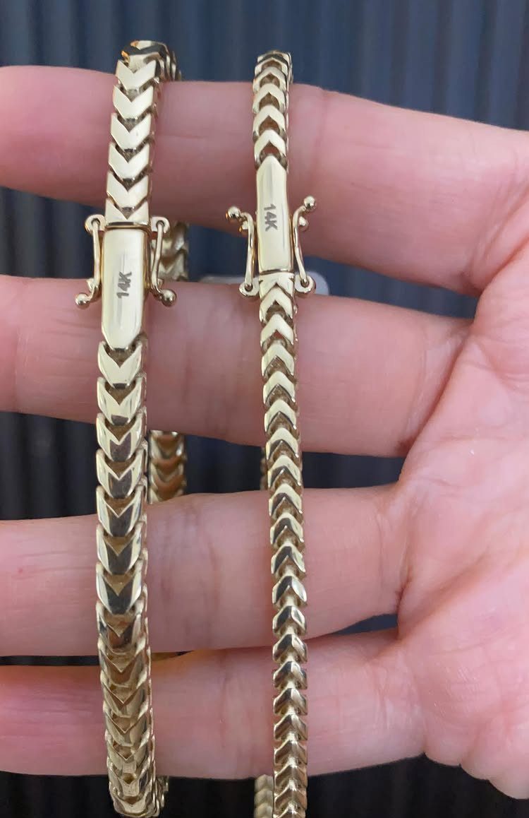 Two gold Franco style bracelets with V-shaped links held in a person's hand.