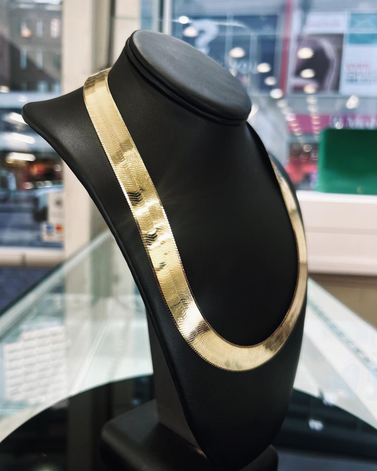 A gold herringbone chain necklace displayed on a black velvet jewelry bust stand.