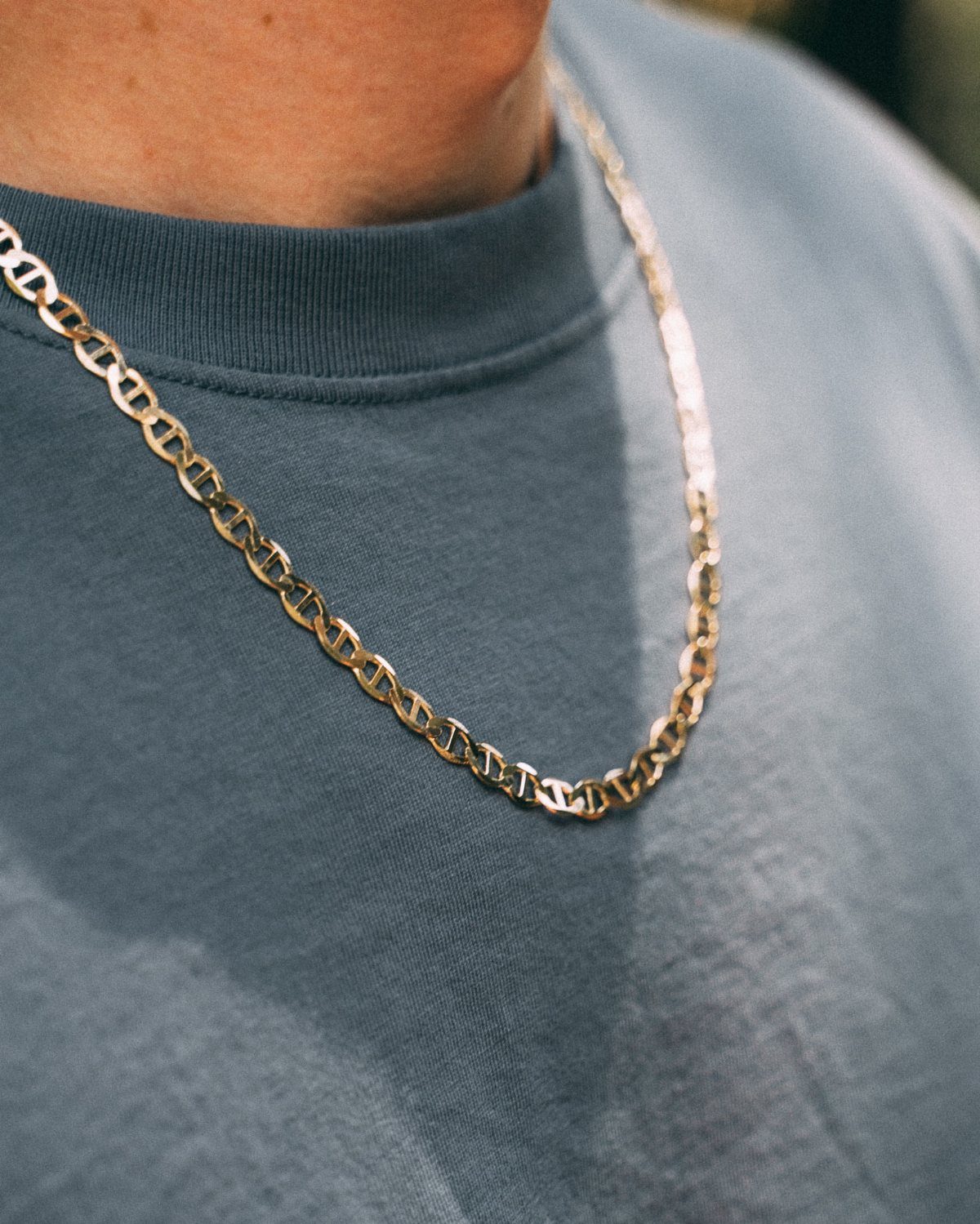 A gold mariner chain necklace worn over a blue crewneck sweatshirt on a person.