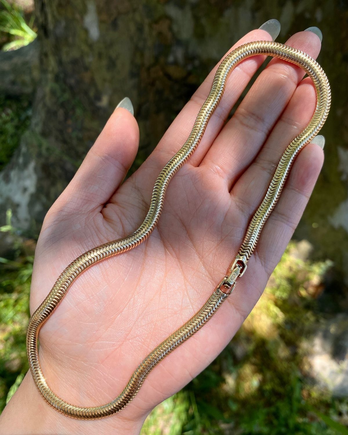A gold snake chain necklace held in an open hand against a natural background.
