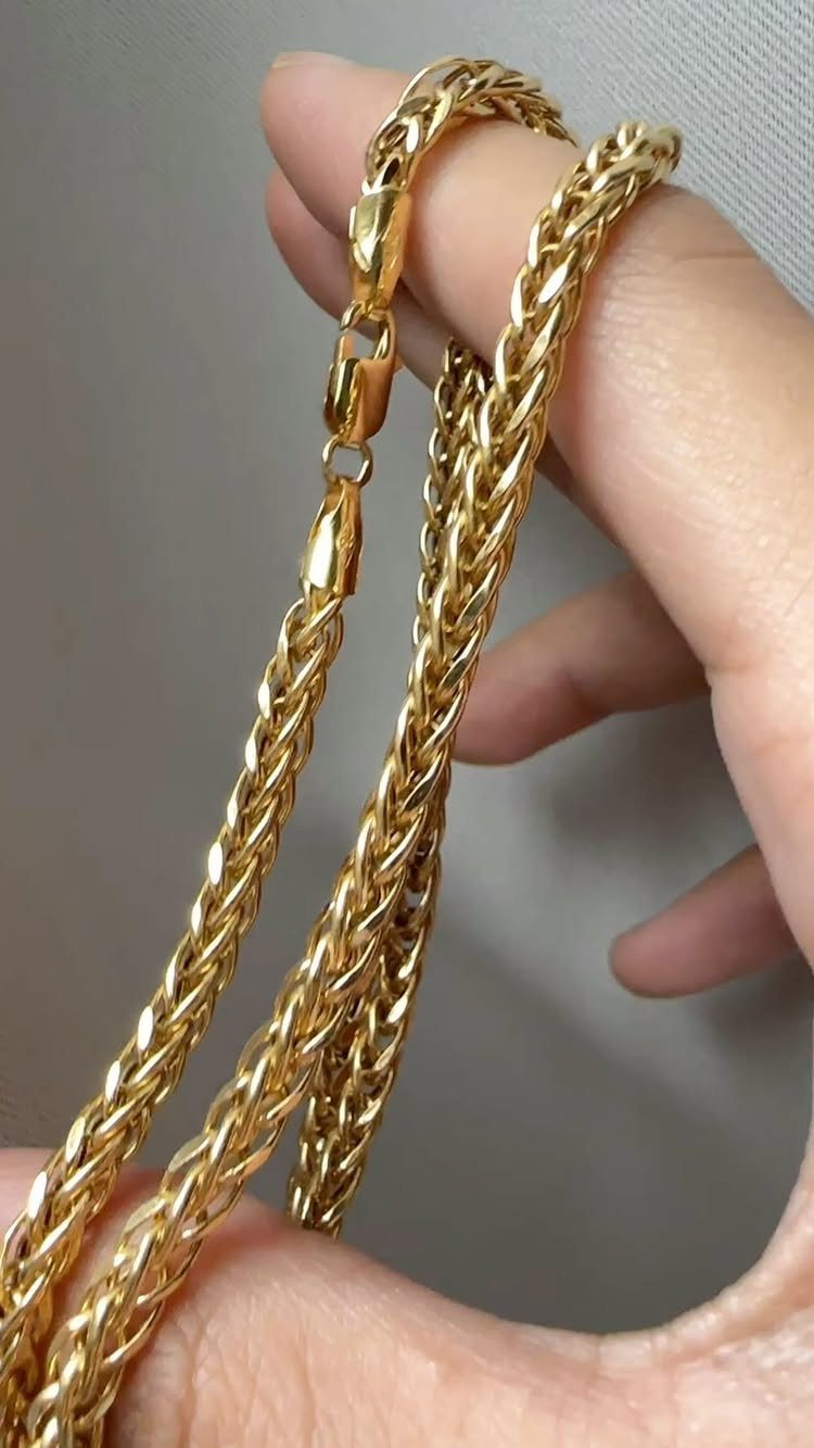 A hand holding a thick, braided gold wheat style chain against a grey background.