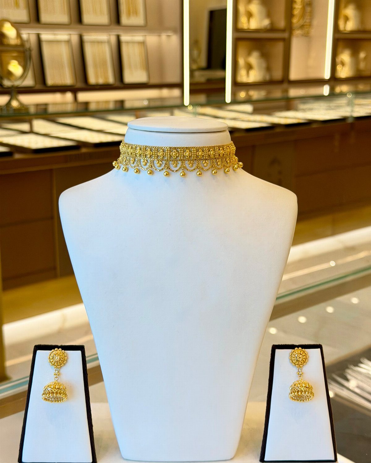Gold choker necklace and matching earrings displayed on white jewelry stands in a store.