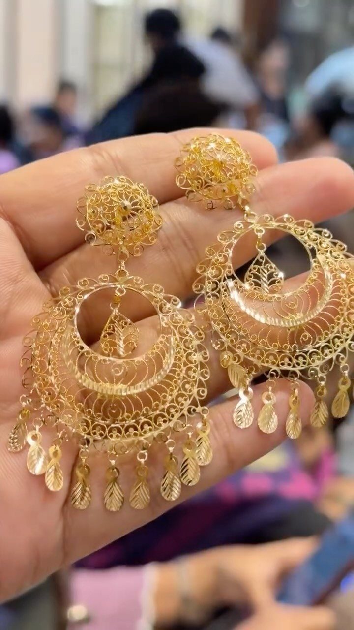 Intricate gold filigree earrings with dangling leaf charms held in a person's hand.