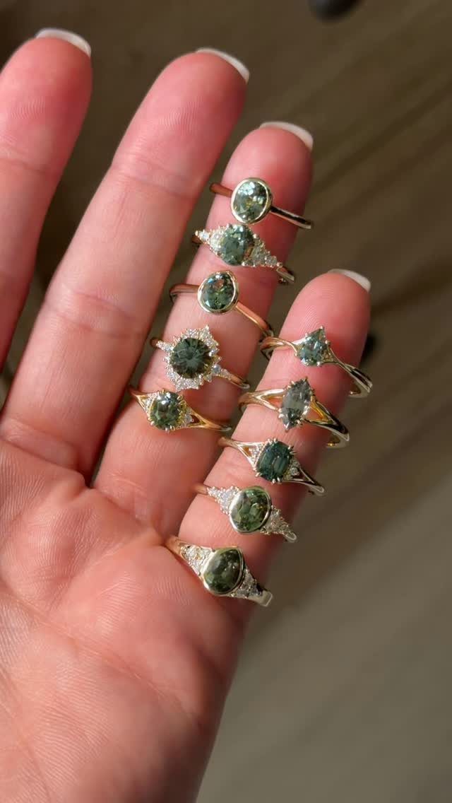 Several gold rings with large green gemstones held in a person's hand.